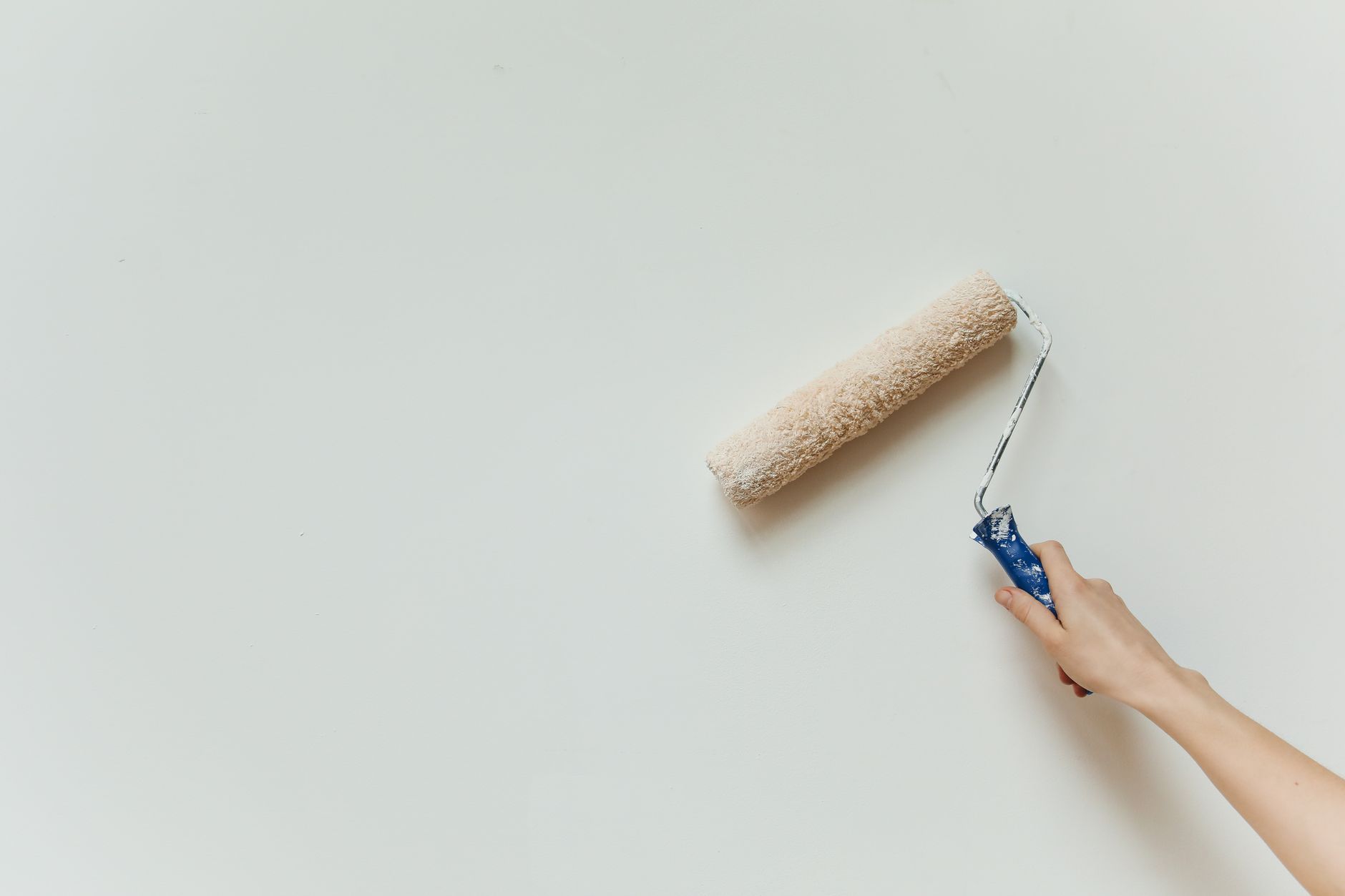 Main qui applique de la peinture au rouleau sur un mur