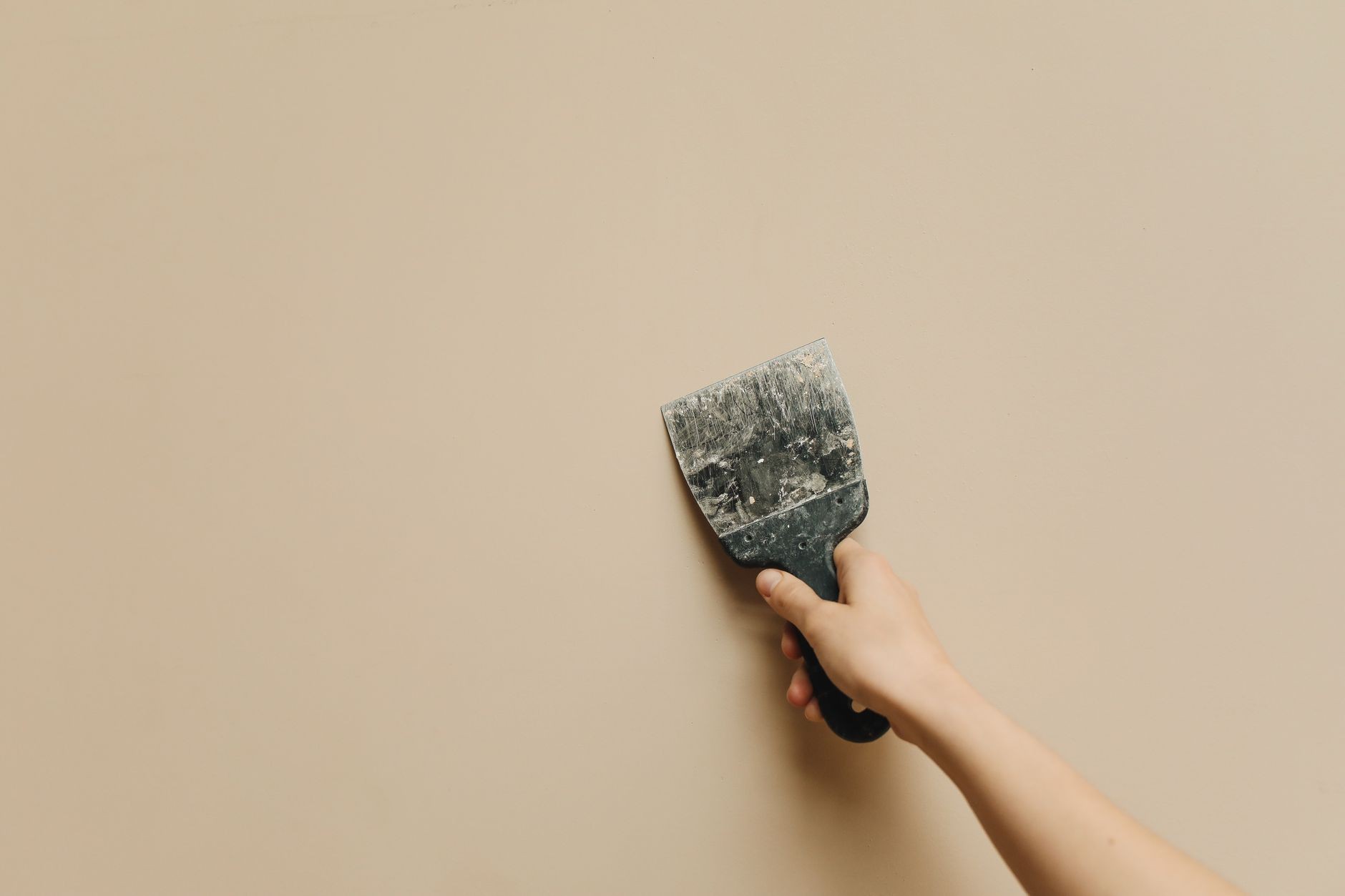 Main avec une spatule sur un mur en rénovation