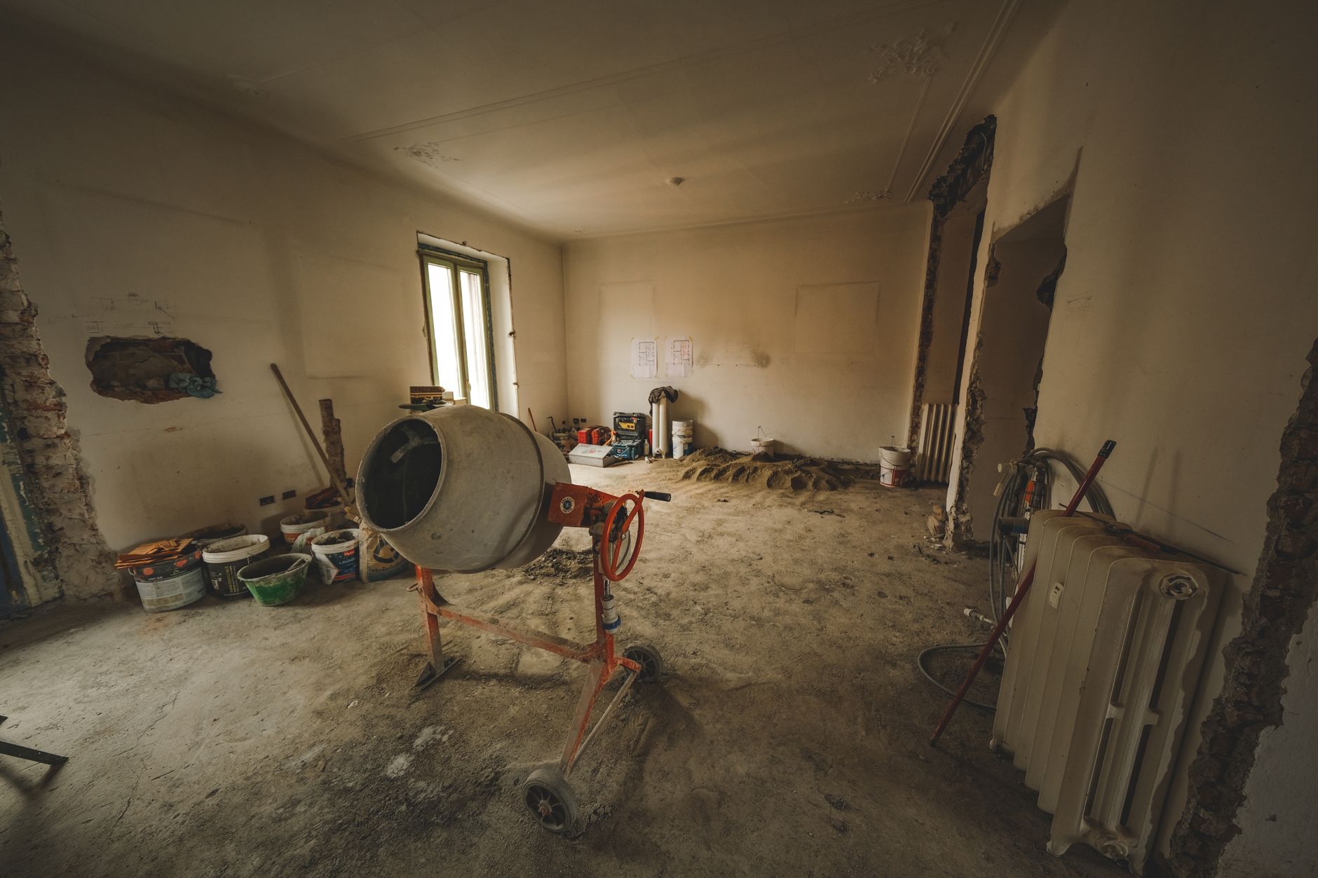 Pièce vide en rénovation avec bétonnière et outils prêts pour un ragréage