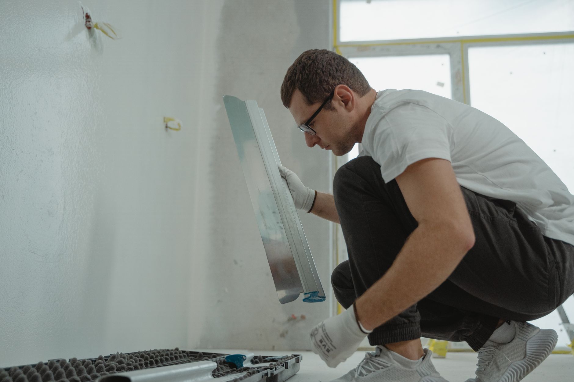 Main qui lisse un enduit à la truelle métallique dans une pièce en rénovation